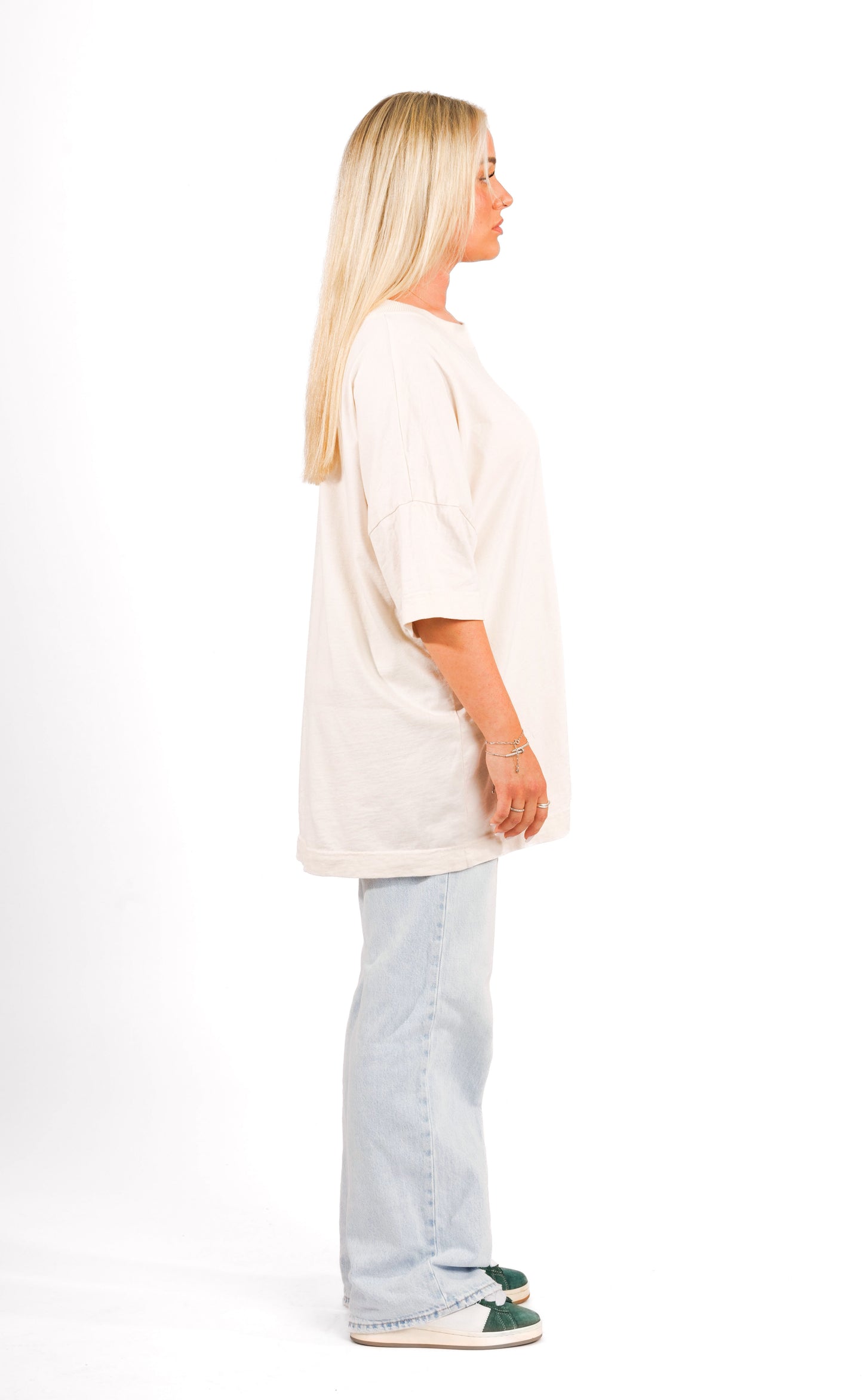 Seitenansicht einer Frau mit blondem Haar, die ein weißes Harry-Potter-T-Shirt trägt, vor einem neutralen weißen Hintergrund.