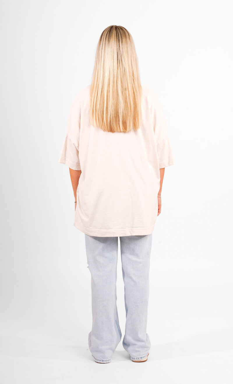 Rückansicht einer Frau mit blondem Haar, die ein weißes Harry-Potter-T-Shirt trägt, vor neutralem, weißem Hintergrund.
